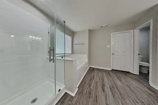 a view of a hallway with wooden floor and a bathroom