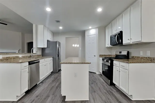 a large kitchen with stainless steel appliances granite countertop a stove top oven a refrigerator a sink and dishwasher with wooden floor