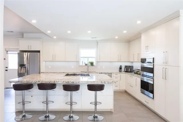 a kitchen with stainless steel appliances kitchen island granite countertop a dining table chairs and white cabinets