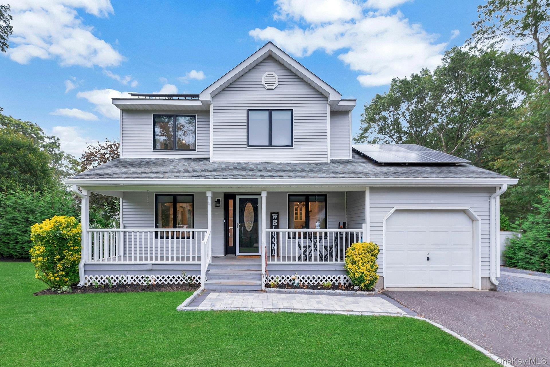 View of front of house featuring a porch, a front lawn, solar panels, a garage, and driveway
