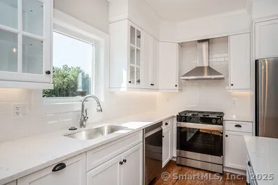 a large white kitchen with wooden floor and a large window