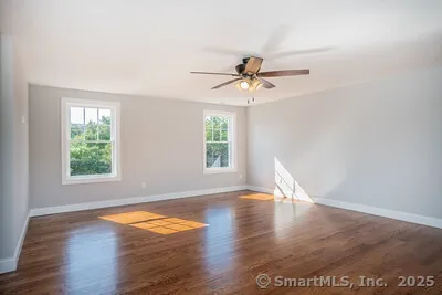 an empty room with wooden floor chandelier fan and windows