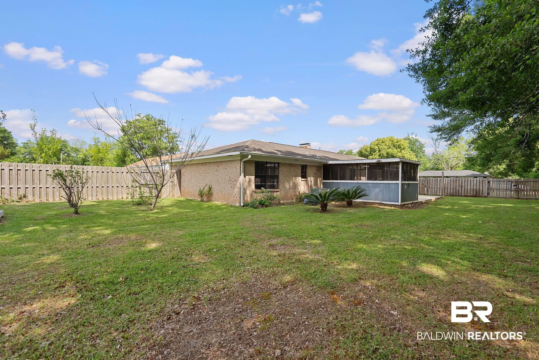 716 North Cedar Street Foley, AL 36535 - Photo 24 of 25 Expansive backyard featuring a manicured lawn, full privacy fencing, brick exterior, and a screened-in patio