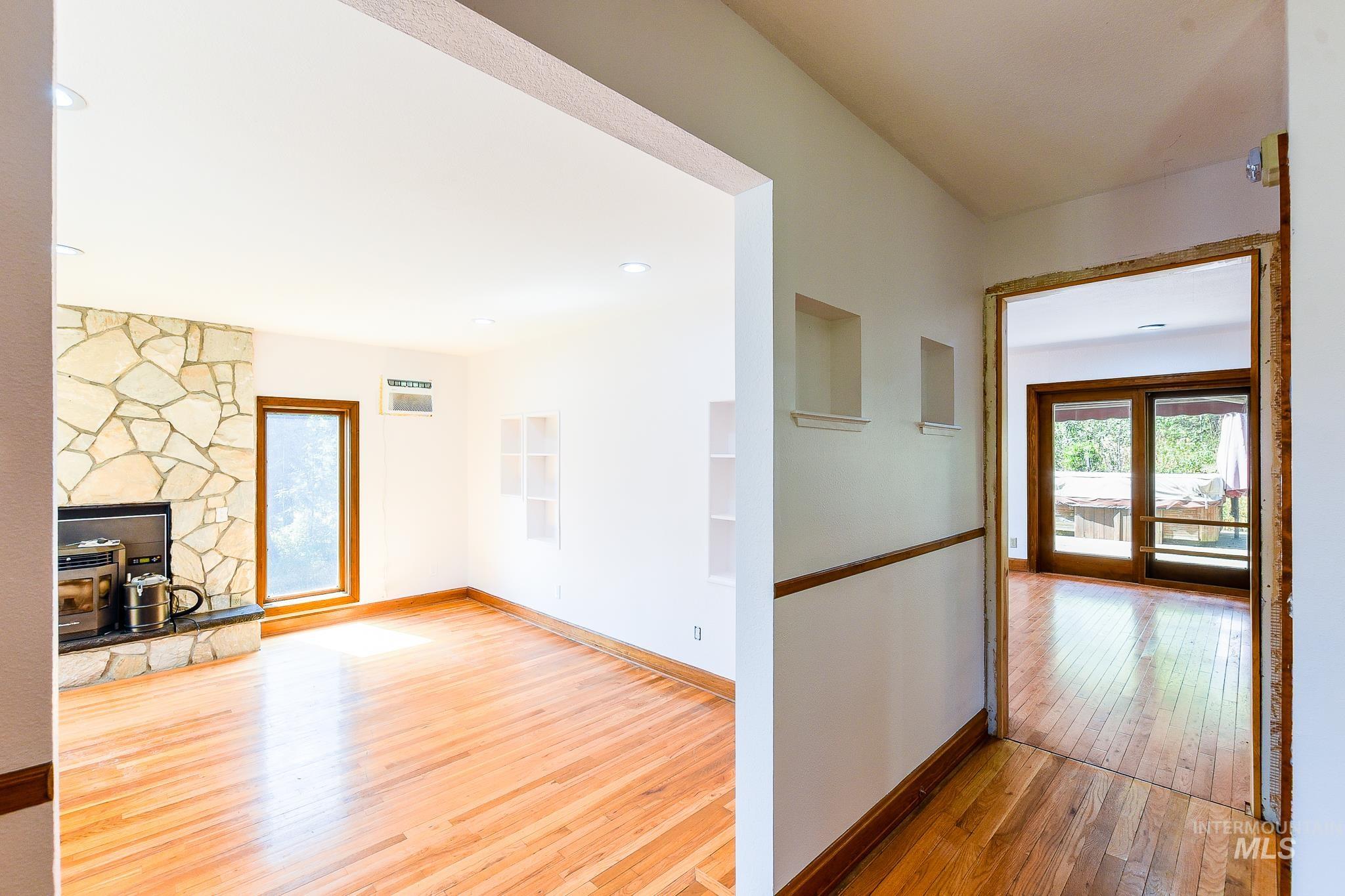Hardwood flooring throughout, a stone-front fireplace with a black hearth, built-in wall niches, and a window with wood trim