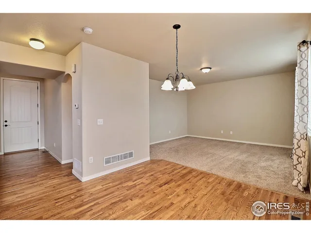 a view of empty room with wooden floor and kitchen view