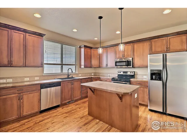 a kitchen with stainless steel appliances kitchen island granite countertop a refrigerator a stove a sink a microwave oven with cabinets and wooden floor