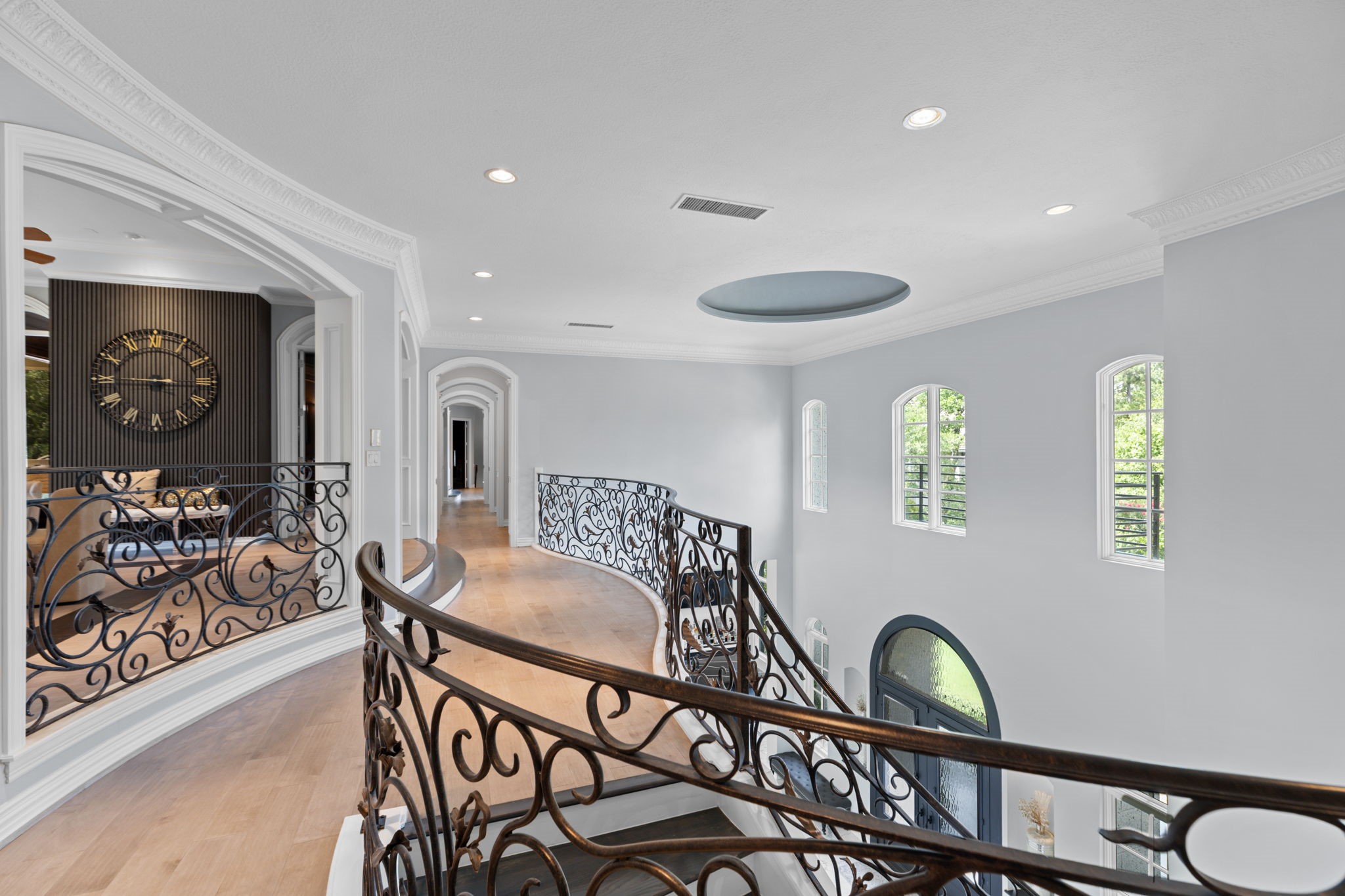 39 Maymont Way Spring, TX 77382 - Photo 25 of 50 This photo showcases a luxurious hallway with elegant wrought iron railings, hardwood floors, and arched windows that allow natural light to fill the space. The curved design and high ceilings add a touch of sophistication, providing a glimpse into a stylish and spacious home.