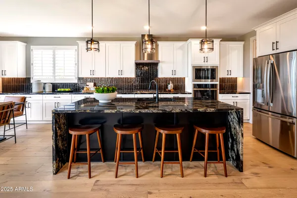 a kitchen with stainless steel appliances granite countertop a stove top oven a refrigerator a sink and chairs