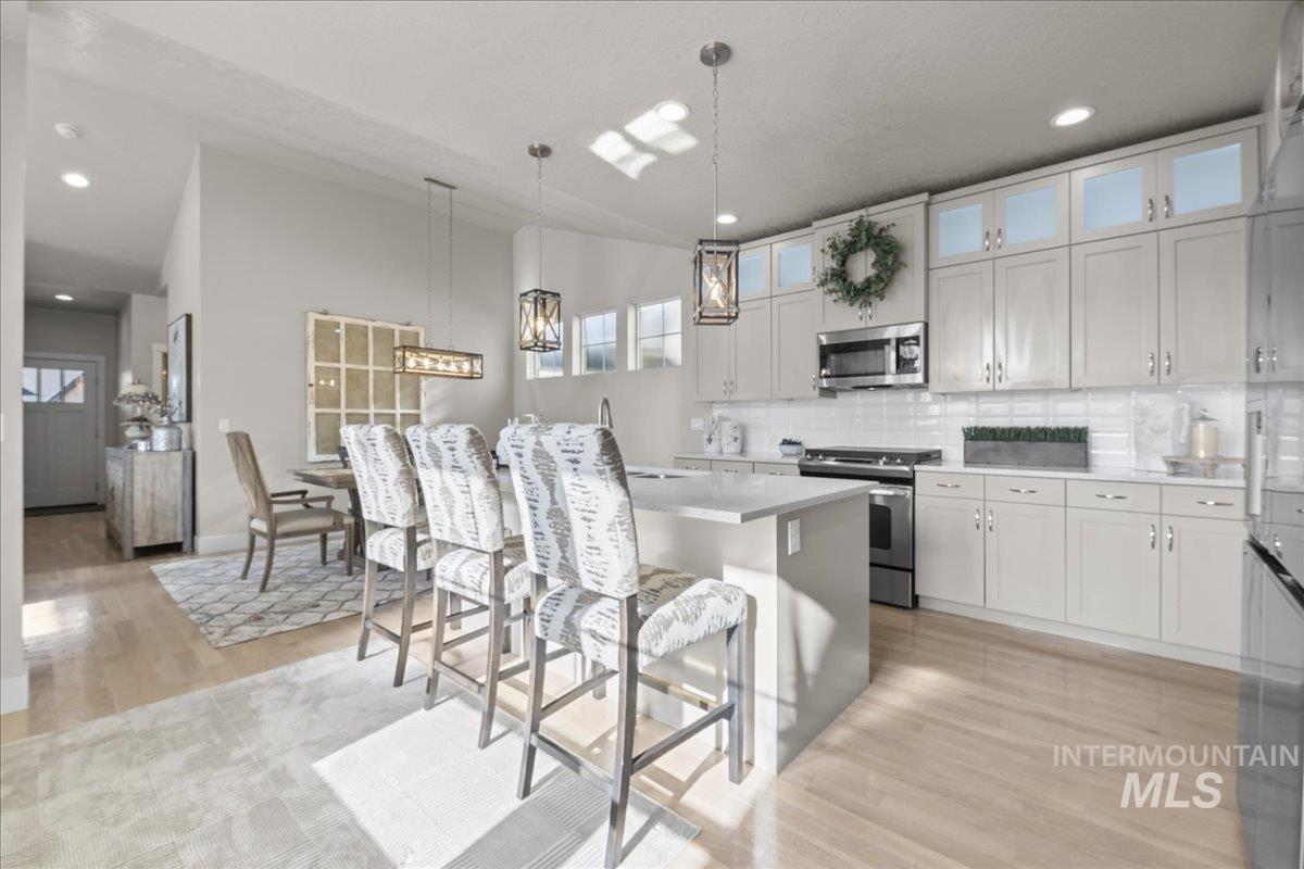 2856 South Wise Way Boise, ID 83716 - Photo 14 of 47 Kitchen featuring pendant lighting, light wood-style flooring, stainless steel appliances, glass insert cabinets, and a breakfast bar