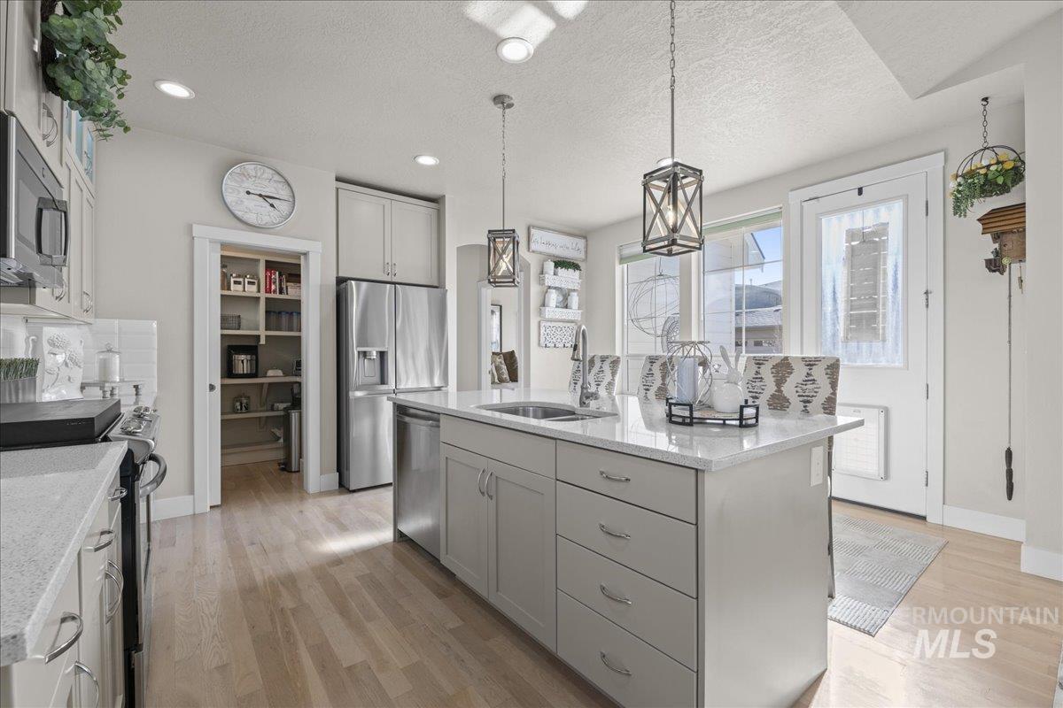 2856 South Wise Way Boise, ID 83716 - Photo 16 of 47 Kitchen featuring stainless steel appliances, hanging light fixtures, gray cabinets, light wood-type flooring, and light stone countertops