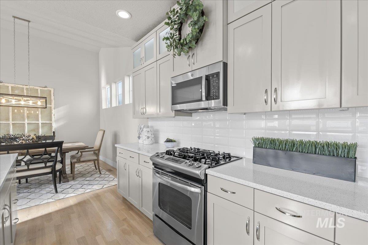 2856 South Wise Way Boise, ID 83716 - Photo 18 of 47 Kitchen featuring stainless steel appliances, light wood-style floors, glass insert cabinets, light stone counters, and tasteful backsplash
