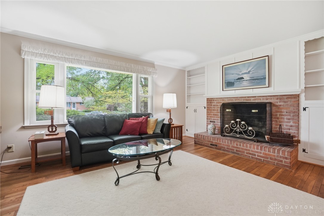 6119 Flemington Road Dayton, OH 45459 - Photo 8 of 76 This inviting living room features a classic brick fireplace and built-in shelving, complemented by rich hardwood flooring.