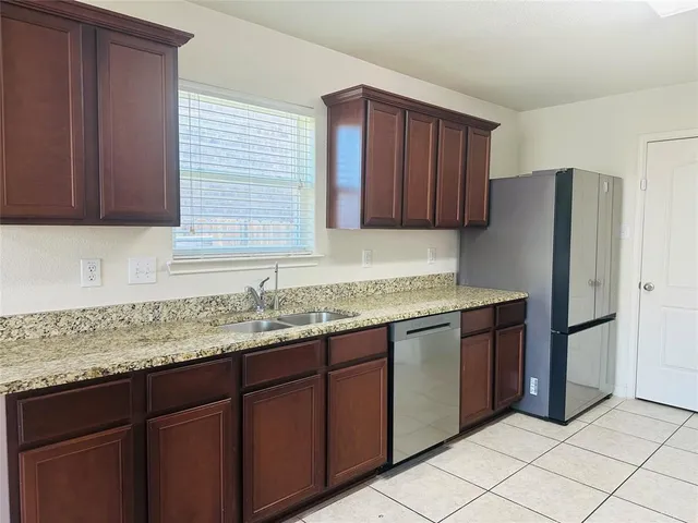 a kitchen with granite countertop wooden cabinets a refrigerator and a sink