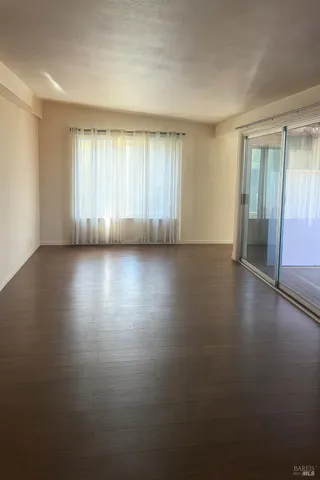 an empty room with wooden floor and windows with curtains
