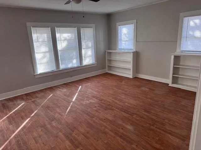 an empty room with wooden floor closet and windows
