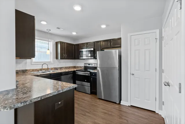 a kitchen with granite countertop stainless steel appliances a refrigerator a sink and wooden cabinets