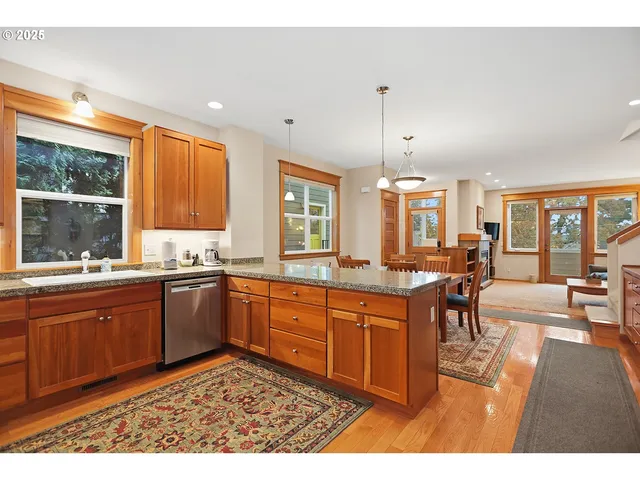 a kitchen with stainless steel appliances granite countertop a stove top oven a sink dishwasher a dining table and chairs with wooden floor