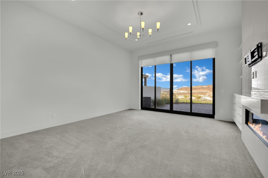 658 Falcon Summit Court Henderson, NV 89012 - Photo 25 of 99 Unfurnished living room with a glass covered fireplace, light colored carpet, and a chandelier