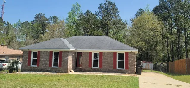 a view of a white house with a large windows and a yard with plants and trees