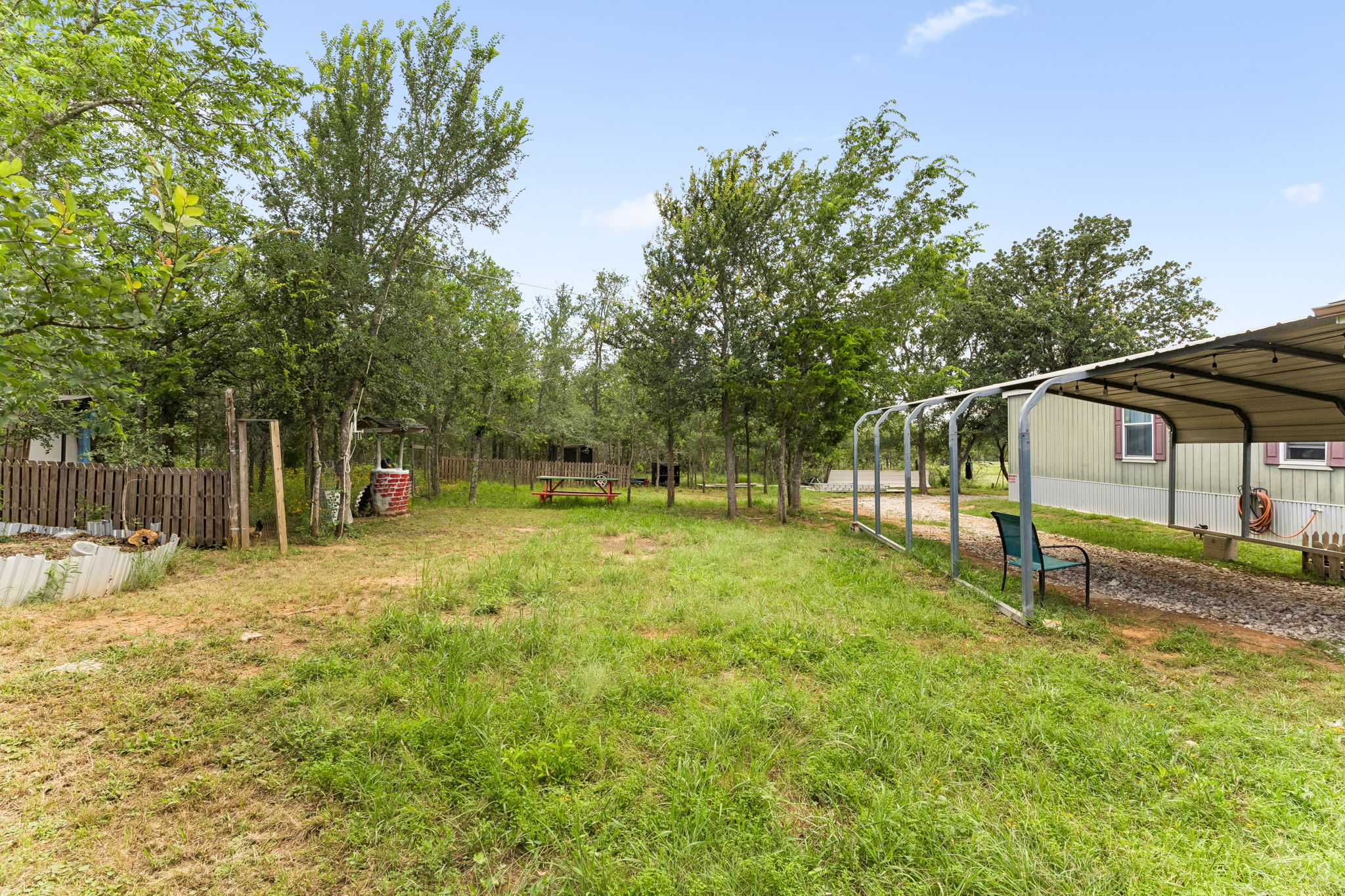 253 North County Line Road, Unit C Elgin, TX 78621 - Photo 27 of 39 A verdant backyard with mature trees and a fenced garden area, offering a serene outdoor escape.