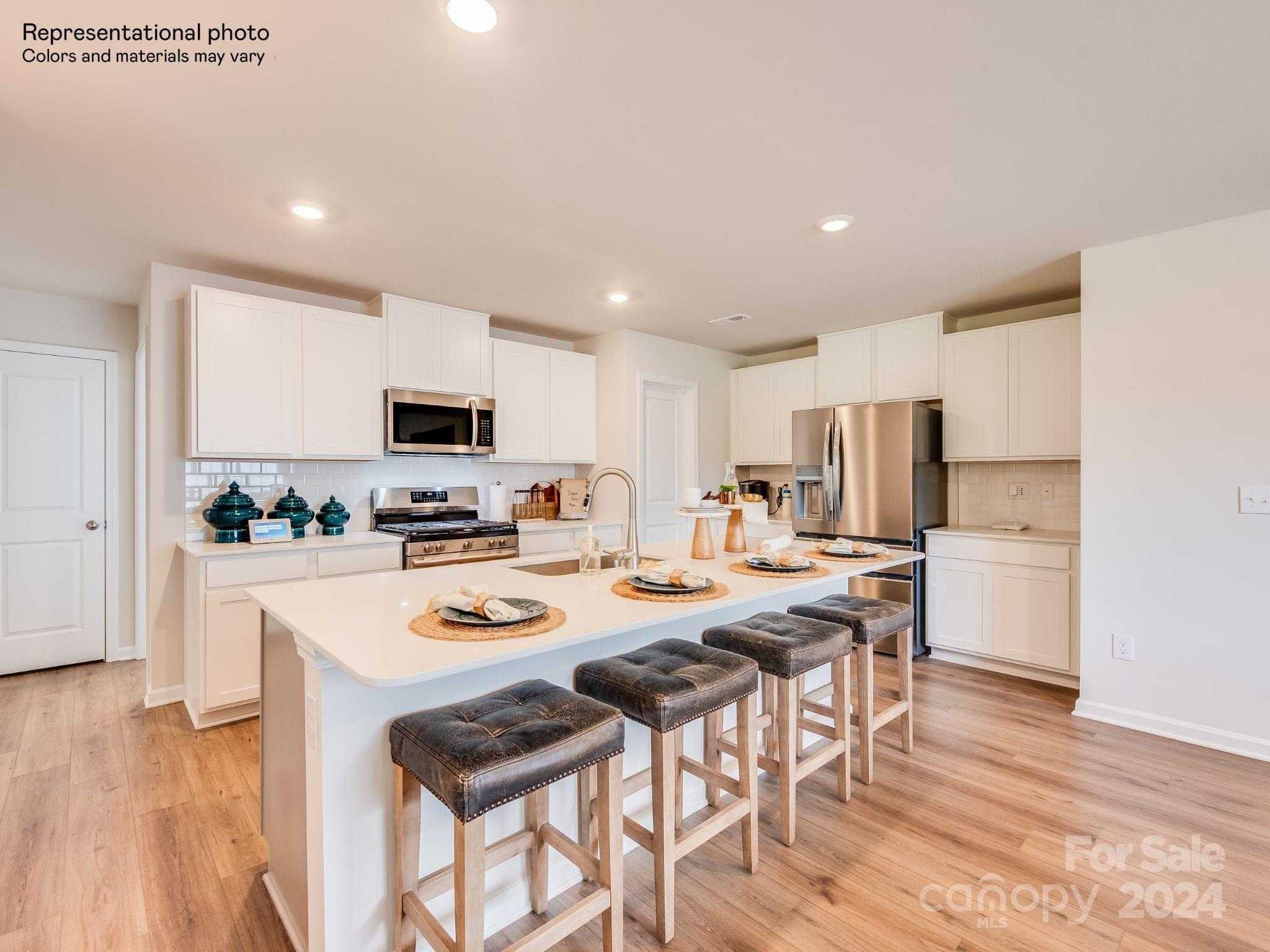 a kitchen with stainless steel appliances a stove top oven a refrigerator a sink and white cabinets with wooden floor