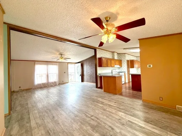 a view of an empty room with a window and kitchen view