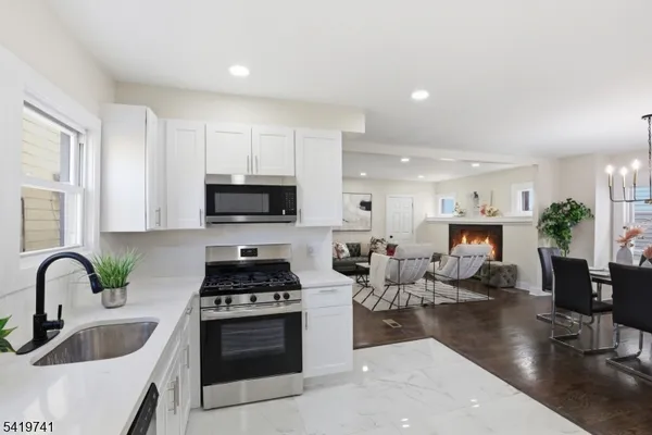 a kitchen with stainless steel appliances a stove a sink a microwave a refrigerator white cabinets a dining table and chairs