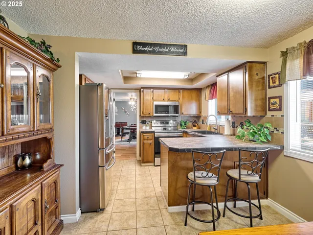 a kitchen with stainless steel appliances kitchen island granite countertop a stove a refrigerator a dining table and chairs with wooden floor