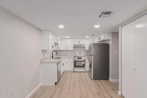 a kitchen with stainless steel appliances granite countertop a refrigerator a sink dishwasher a stove and white countertops with wooden floor