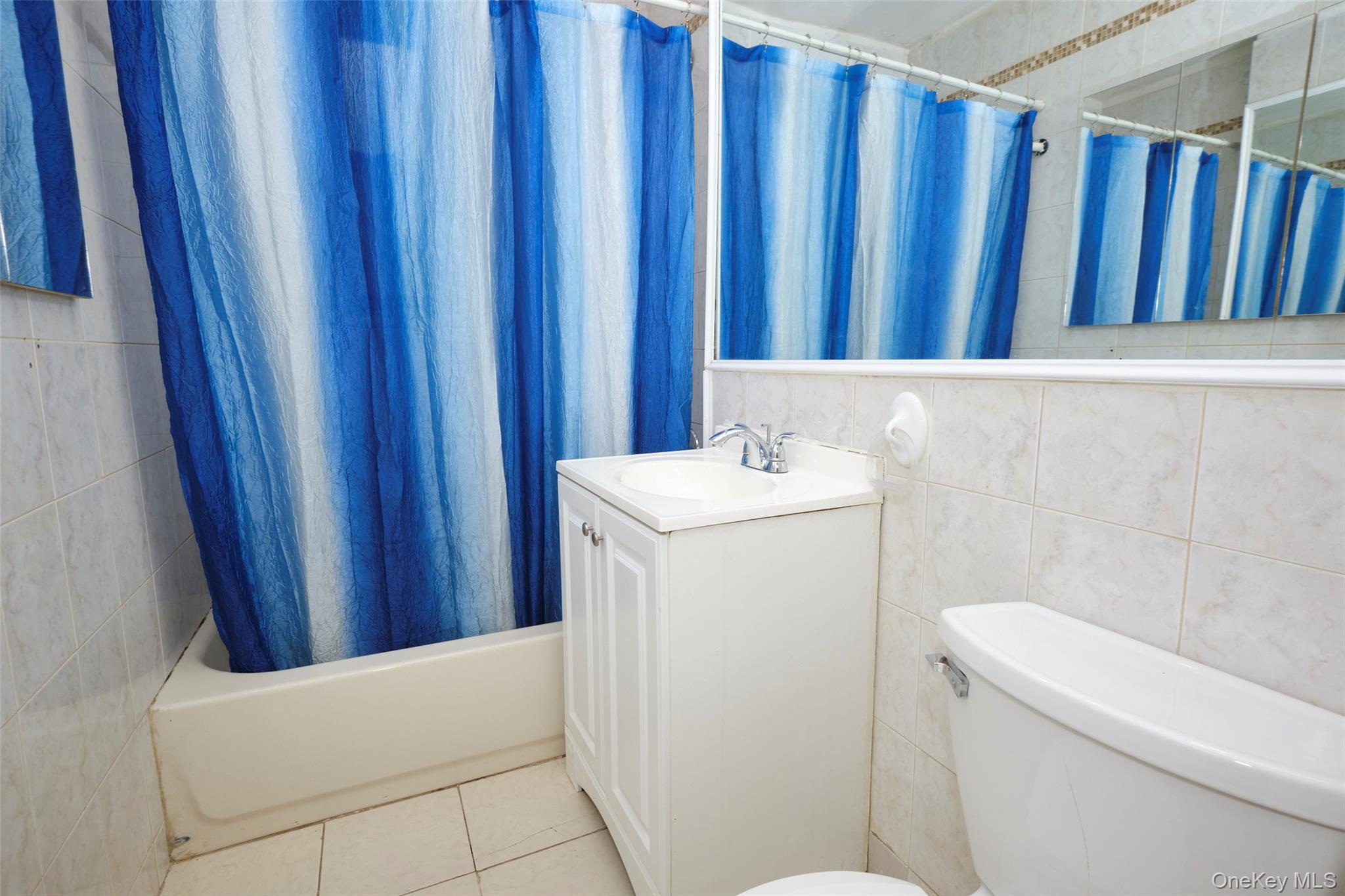 150-11 72nd Road, Unit 1C Queens, NY 11367 - Photo 14 of 25 Bathroom with tile walls, vanity, shower / bathtub combination with curtain, and light tile patterned floors