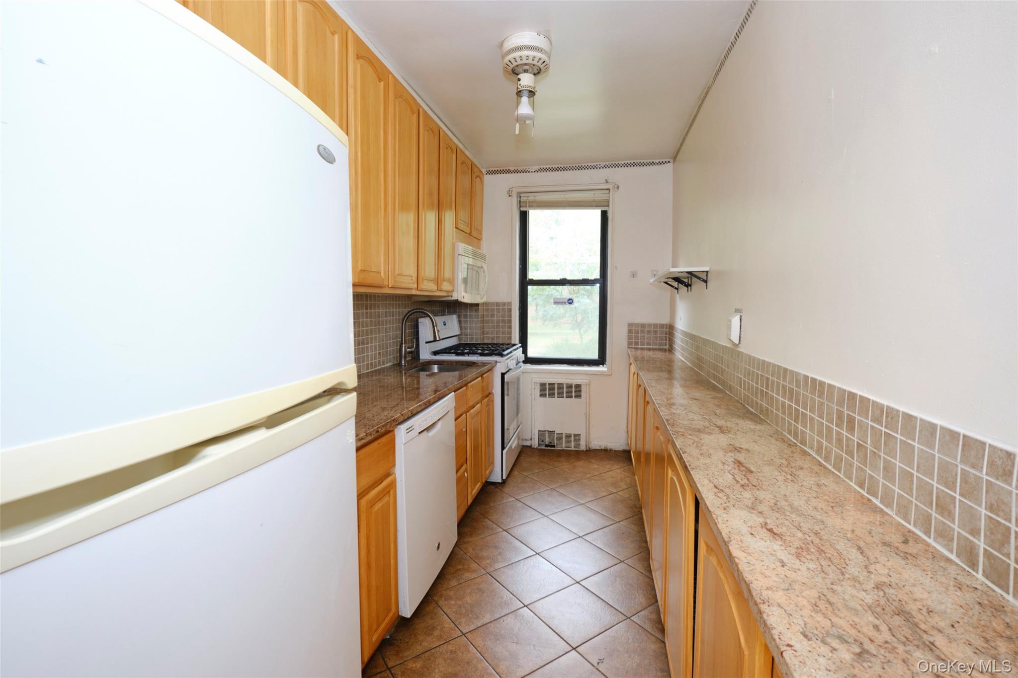 150-11 72nd Road, Unit 1C Queens, NY 11367 - Photo 7 of 25 Kitchen with white appliances, backsplash, light tile patterned flooring, radiator, and dark stone countertops