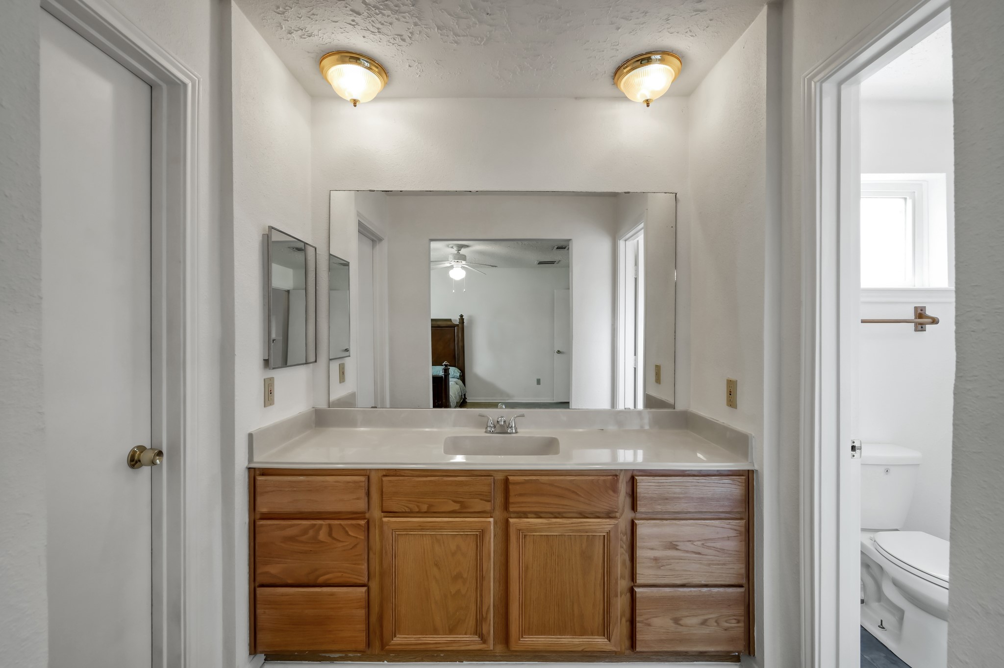 4314 Enchantedgate Drive Spring, TX 77373 - Photo 25 of 47 En-suite bathroom with a large mirror above a wooden vanity with ample storage. The space is well-lit with two ceiling lights, and there's a glimpse of a separate toilet area to the right.