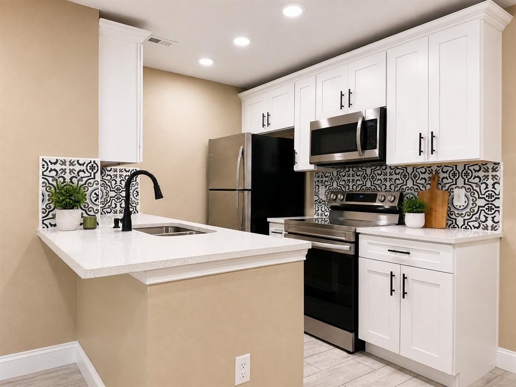 12802 Midway Road, Unit 2015 Dallas, TX 75244 - Photo 1 of 14 White shaker-style cabinetry with matte black hardware, stainless steel appliances, patterned backsplash, quartz countertops, and wood-finish flooring