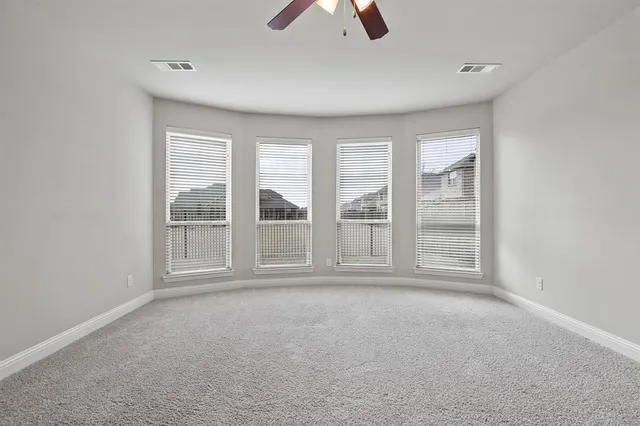 an empty room with chandelier fan and windows