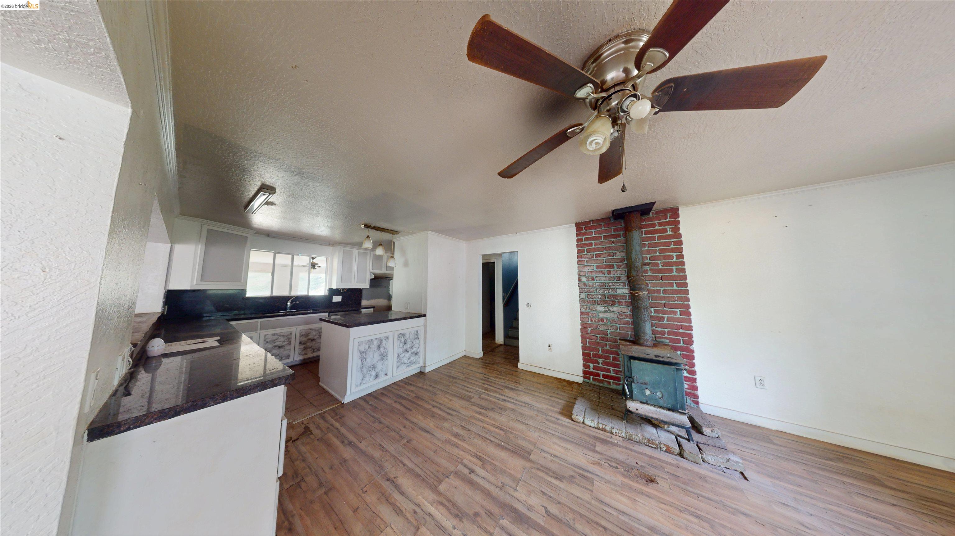 20231 Hidden Acres Road Sonora, CA 95370 - Photo 11 of 25 Open-concept living area featuring wood-finish flooring, a ceiling fan, and a brick-surround wood-burning stove