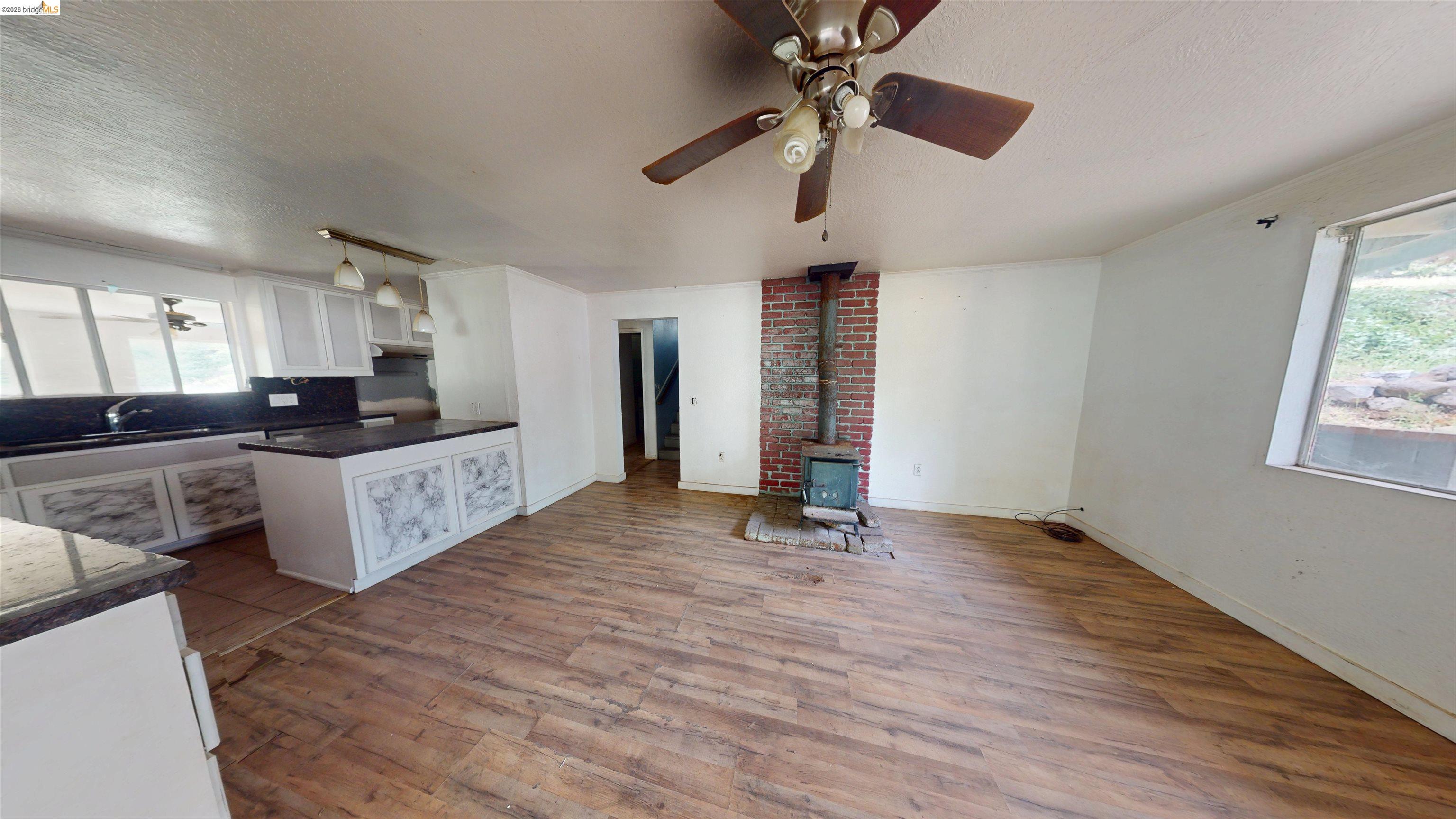 20231 Hidden Acres Road Sonora, CA 95370 - Photo 14 of 25 Open-concept living area with wood-finish flooring, a brick-surround wood stove, and a ceiling fan