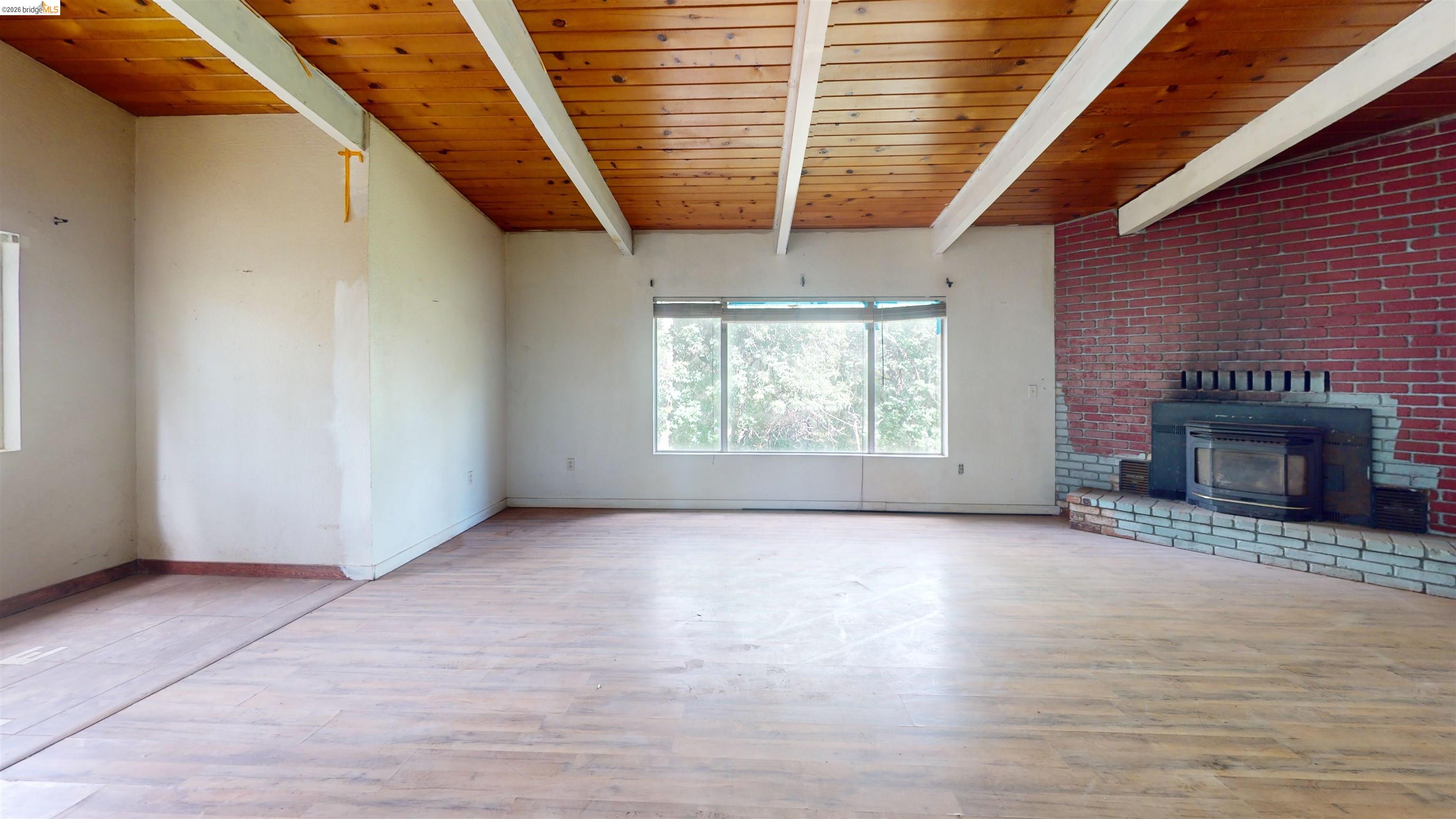 20231 Hidden Acres Road Sonora, CA 95370 - Photo 8 of 25 Spacious interior featuring a wood-finish ceiling with exposed white beams, a large brick accent wall, and a built-in fireplace insert