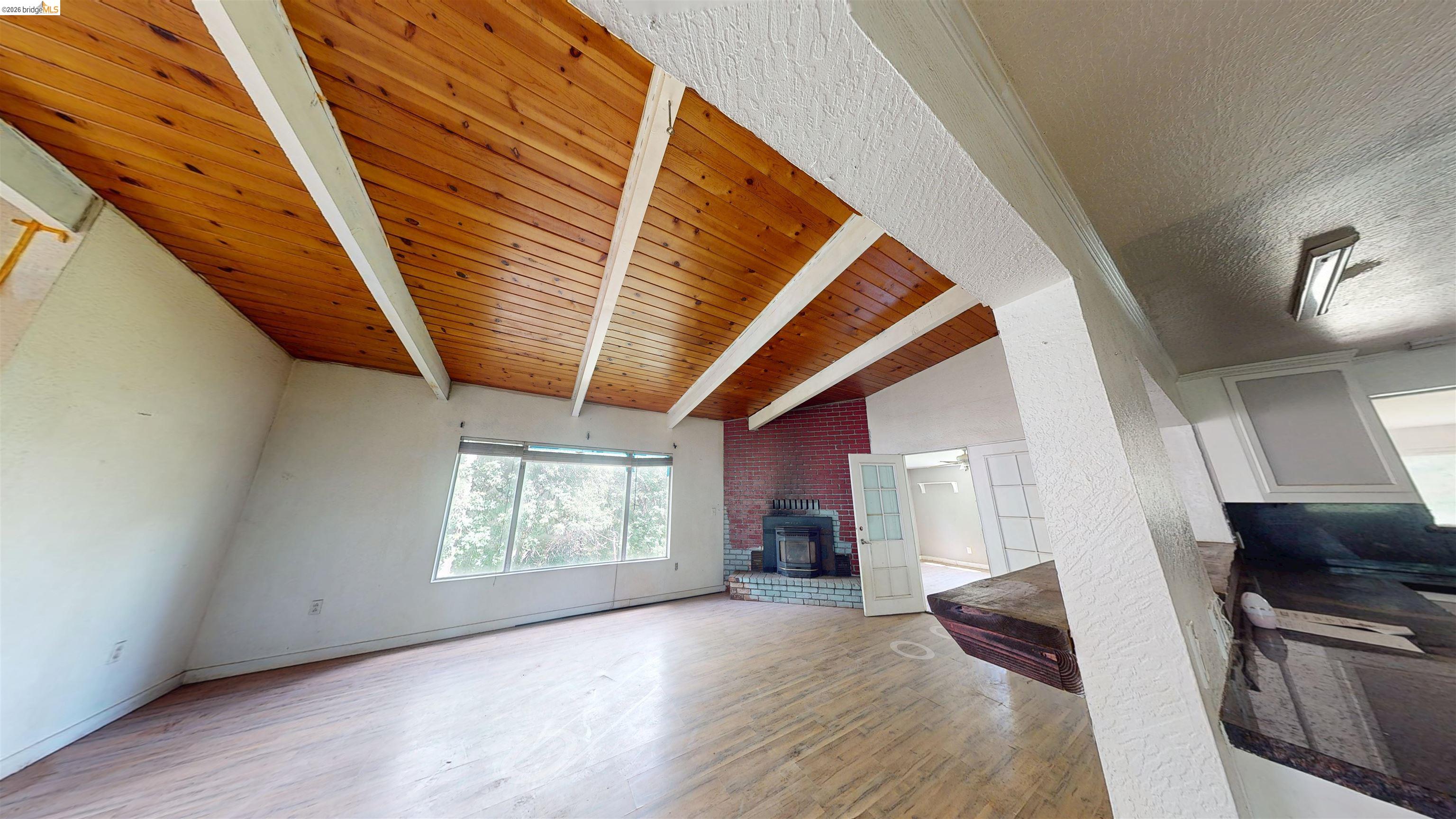 20231 Hidden Acres Road Sonora, CA 95370 - Photo 10 of 25 Spacious interior featuring a vaulted wood-plank ceiling with exposed beams, wood-finish flooring, and a brick fireplace with a raised hearth