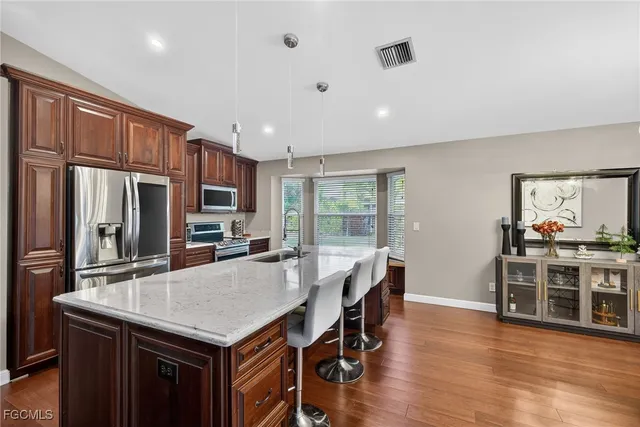 a kitchen with stainless steel appliances granite countertop a stove a refrigerator a kitchen island and chairs with wooden floor