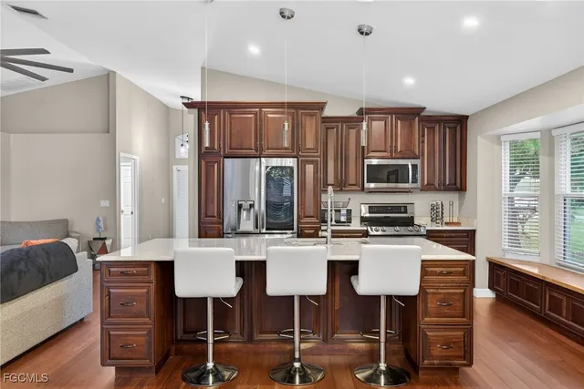 a kitchen with stainless steel appliances granite countertop a stove top oven a refrigerator a dining table and chairs with wooden floor