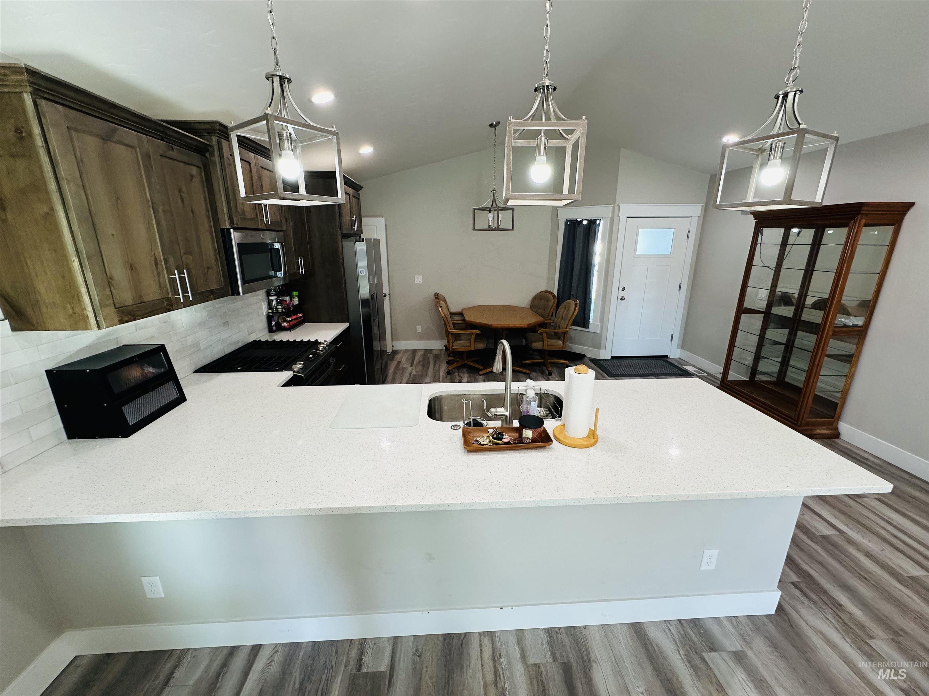 911 Campbell Street Vale, OR 97918 - Photo 5 of 37 Kitchen featuring a peninsula, light stone counters, stainless steel appliances, dark wood-style floors, and vaulted ceiling