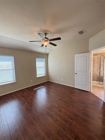 an empty room with wooden floor fan and windows