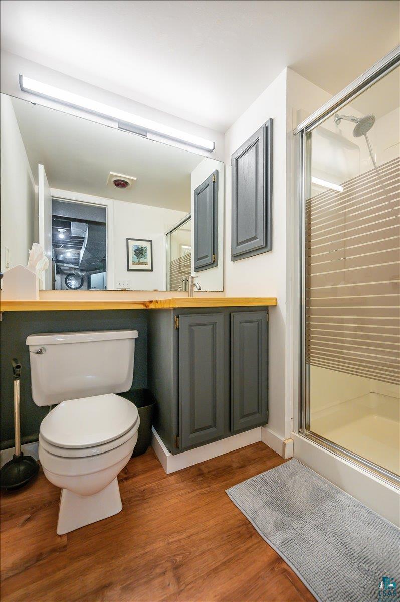 5401 Otsego Street Duluth, MN 55804 - Photo 19 of 36 Bathroom featuring wood-finish flooring, a white toilet, and a glass-enclosed shower