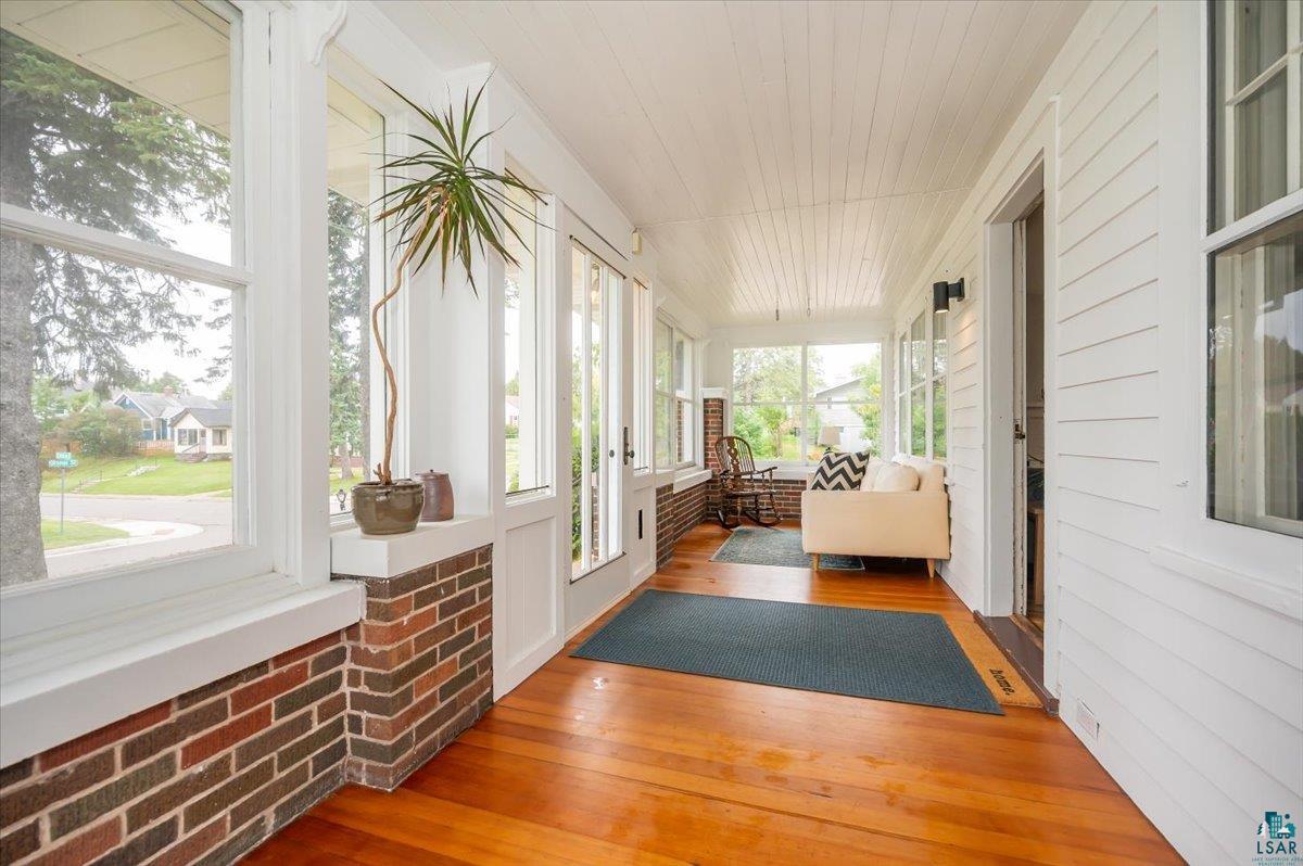 5401 Otsego Street Duluth, MN 55804 - Photo 2 of 36 Sunroom featuring wood-finish flooring, white shiplap ceiling, brick lower wall, large windows, and white vertical paneling