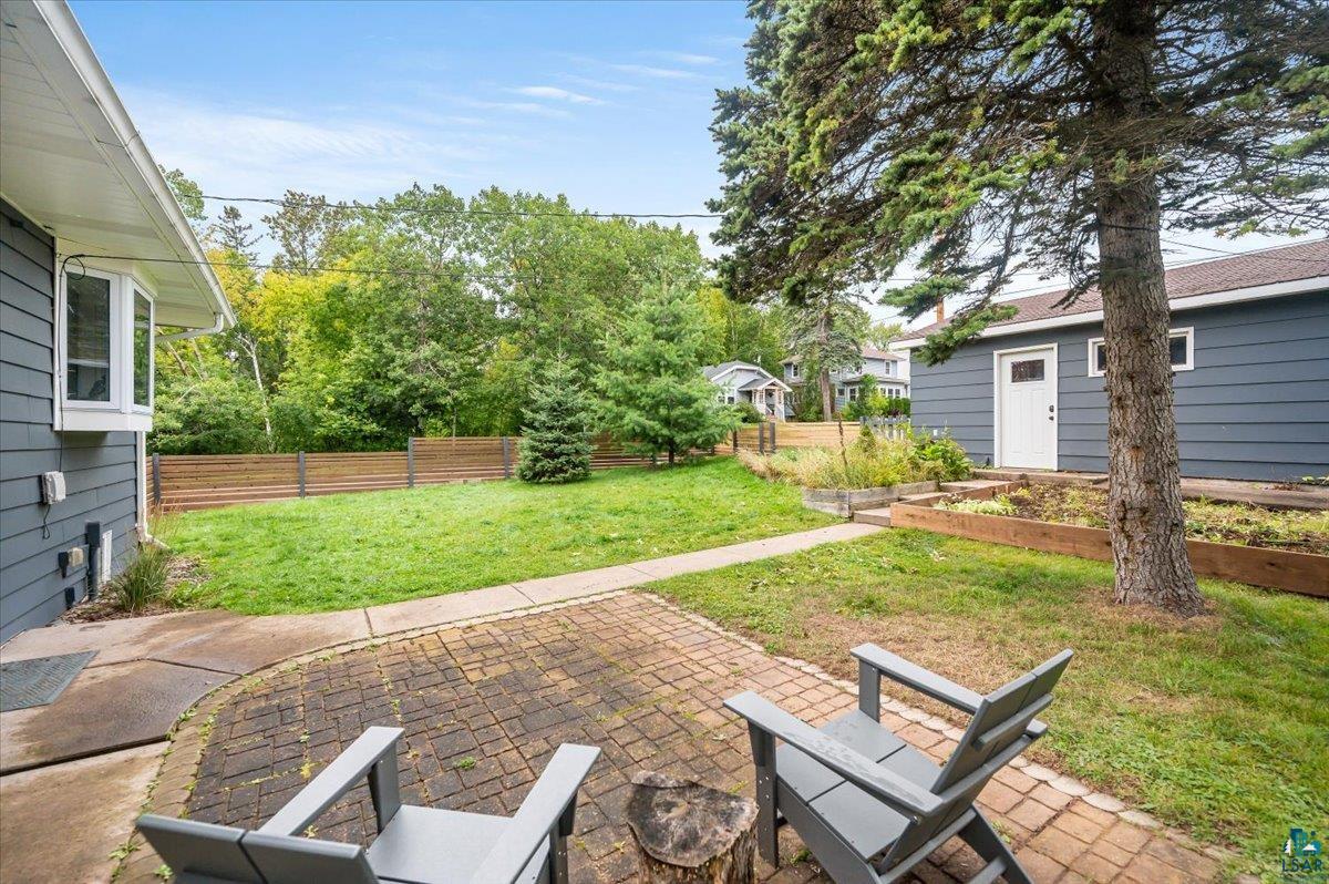 5401 Otsego Street Duluth, MN 55804 - Photo 24 of 36 Brick paver patio with a stone tree stump, a gray wood-paneled exterior, a bay window, and a wooden privacy fence