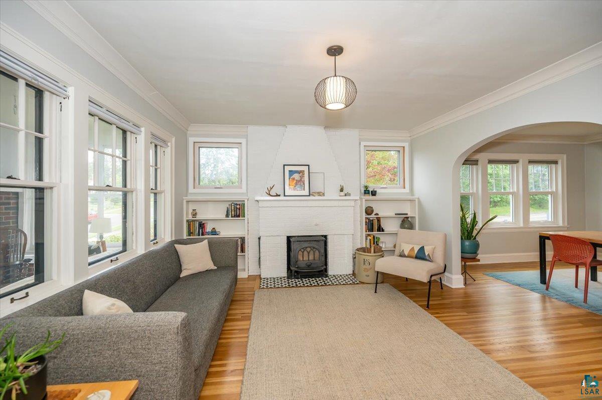 5401 Otsego Street Duluth, MN 55804 - Photo 4 of 36 Living area featuring polished hardwood flooring, a fireplace with a white brick surround, built-in shelving, a decorative pendant light fixture, and multiple windows