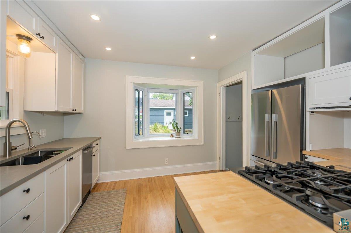 5401 Otsego Street Duluth, MN 55804 - Photo 9 of 36 Kitchen featuring a bay window, recessed lighting, stainless steel appliances, wood-finish flooring, and white cabinetry