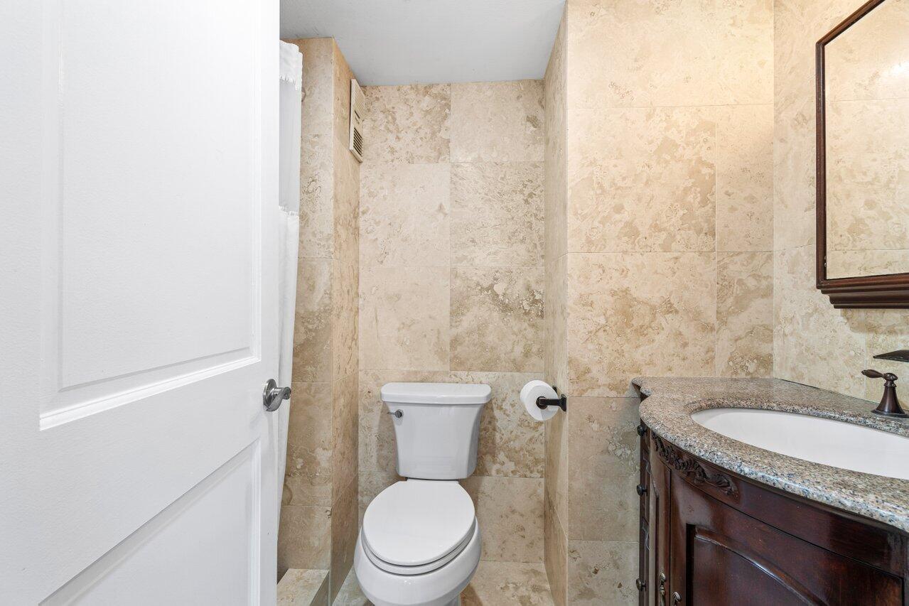 4511 South Ocean Boulevard, Unit 106 Highland Beach, FL 33487 - Photo 18 of 37 a bathroom with a granite countertop toilet a sink and a mirror