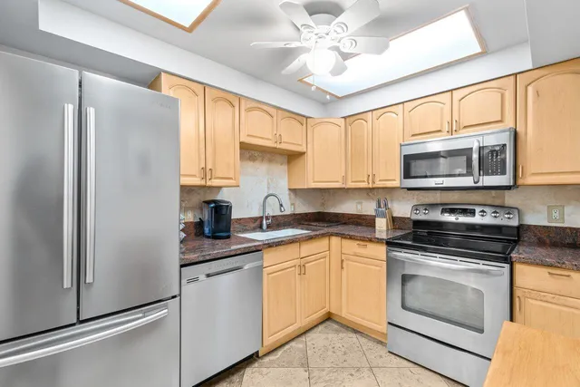 a kitchen with stainless steel appliances granite countertop white cabinets a sink a stove a refrigerator with grey cabinets