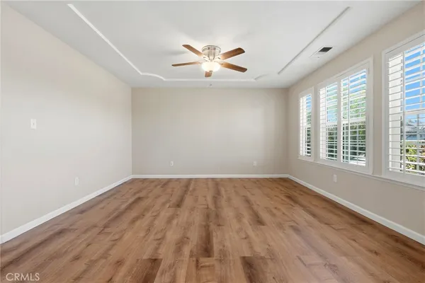 an empty room with wooden floor fan and windows